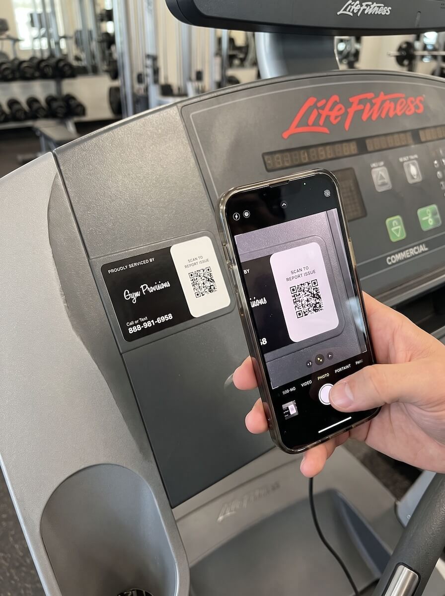 Member scanning a 'Proudly Serviced By' QR sticker on a Life Fitness machine to report an issue